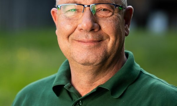 Mann lächelt, trägt eine grüne Polohemd mit Aufschrift „Jägervereinigung Esslingen e.V.“, im Freien mit verschwommenem Hintergrund.