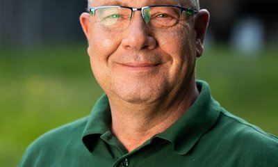 Mann lächelt, trägt eine grüne Polohemd mit Aufschrift „Jägervereinigung Esslingen e.V.“, im Freien mit verschwommenem Hintergrund.