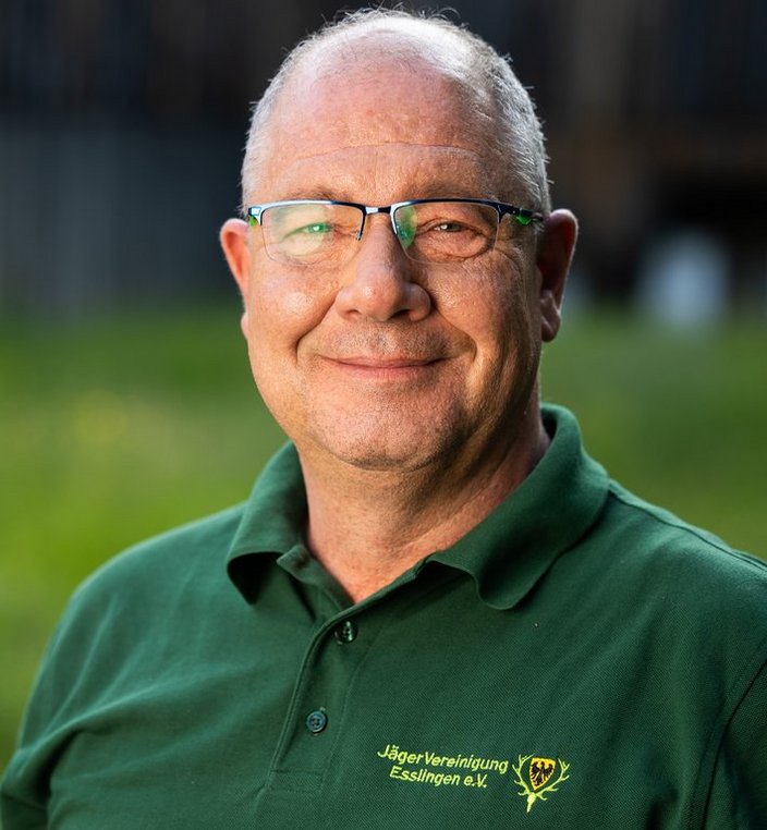 Mann lächelt, trägt eine grüne Polohemd mit Aufschrift „Jägervereinigung Esslingen e.V.“, im Freien mit verschwommenem Hintergrund.